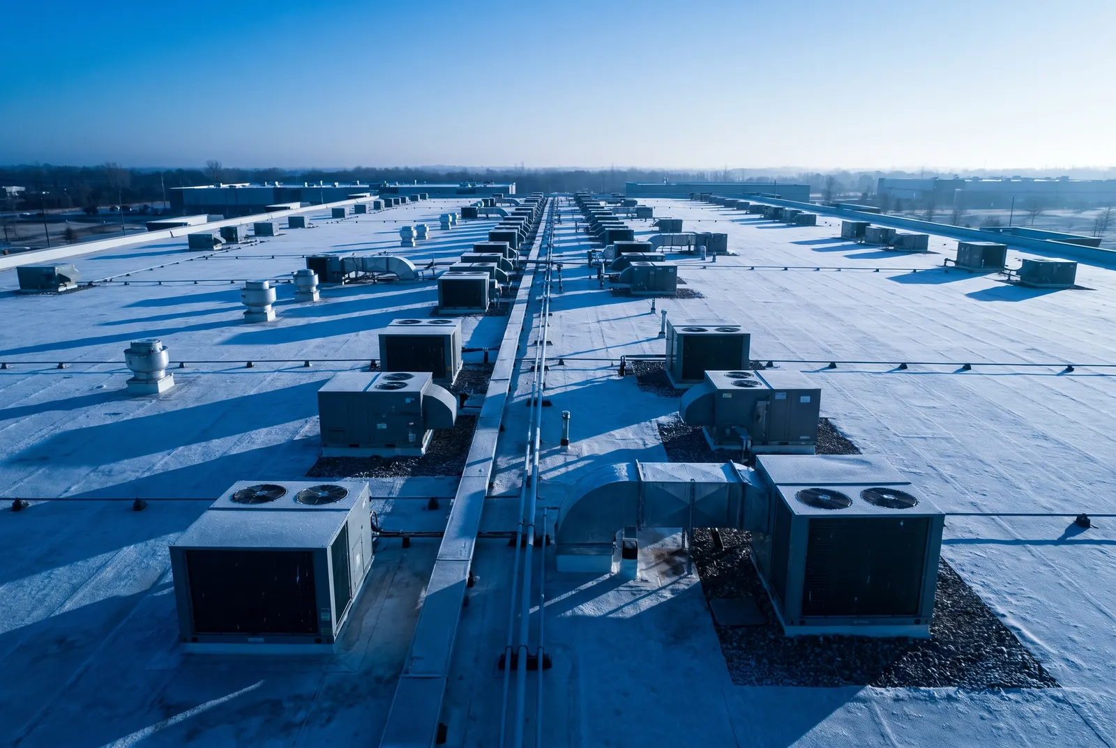 Rows of rooftop HVAC units on a frosted commercial roof at dawn